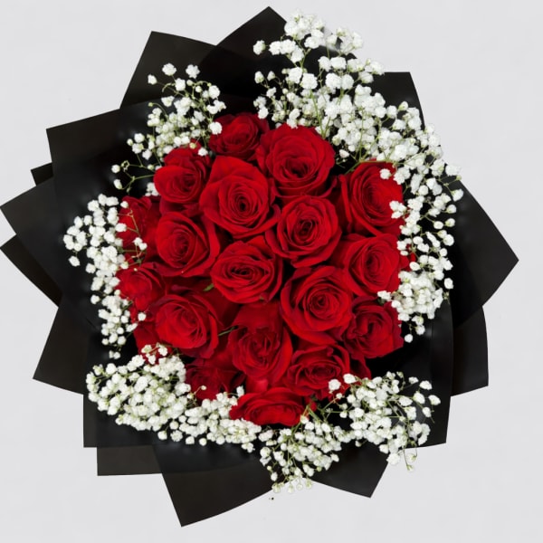 Round bouquet of red roses and white filler flowers wrapped in black paper.