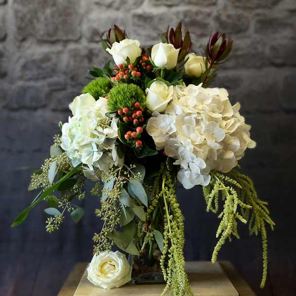 White rose and hydrangea arrangement with trailing greenery in a glass vase