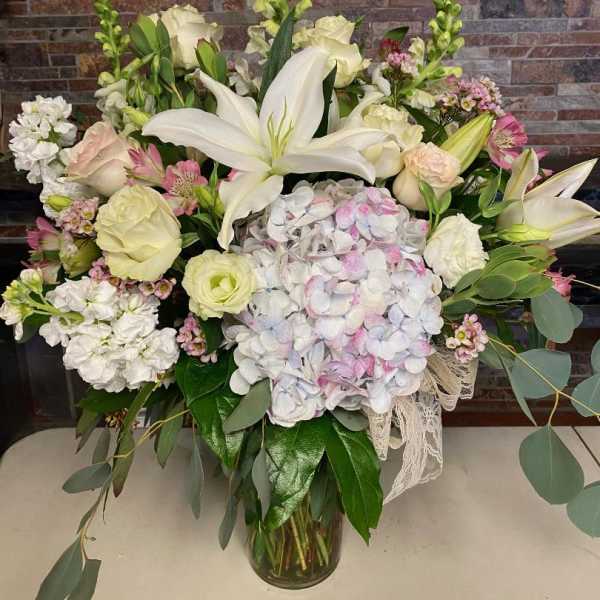 Large bouquet of white lilies, roses, and pastel hydrangeas in a glass vase
