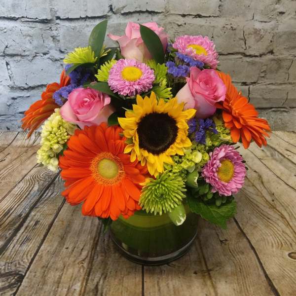 Mixed bouquet with pink roses, sunflowers, and colorful daisies in a glass vase
