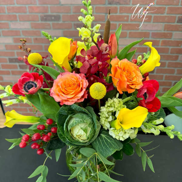 Bright mixed bouquet with orange roses, yellow calla lilies, and red blooms in a glass vase