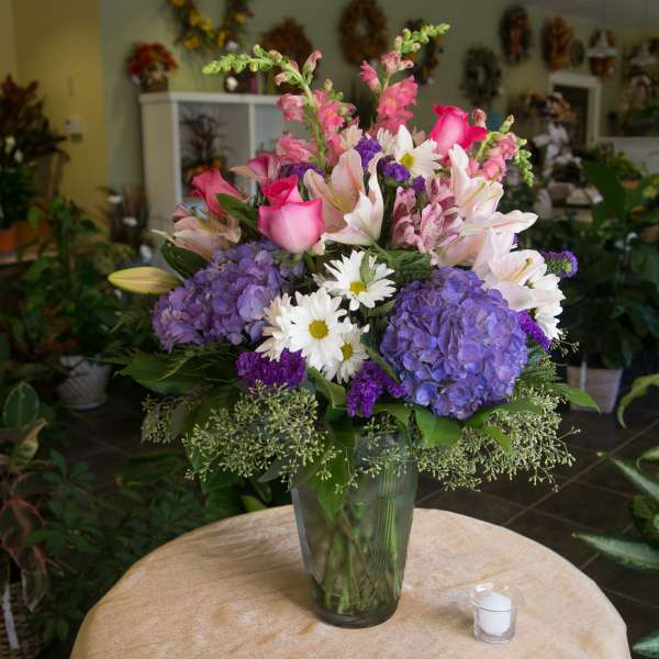 Mixed bouquet of pink roses, lilies, daisies, and purple hydrangeas in a glass vase