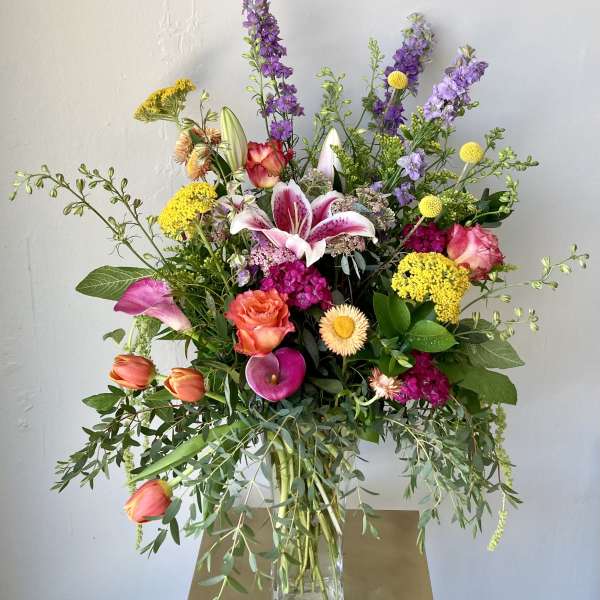 Mixed bouquet with lilies, roses, tulips, and purple spikes in a glass vase