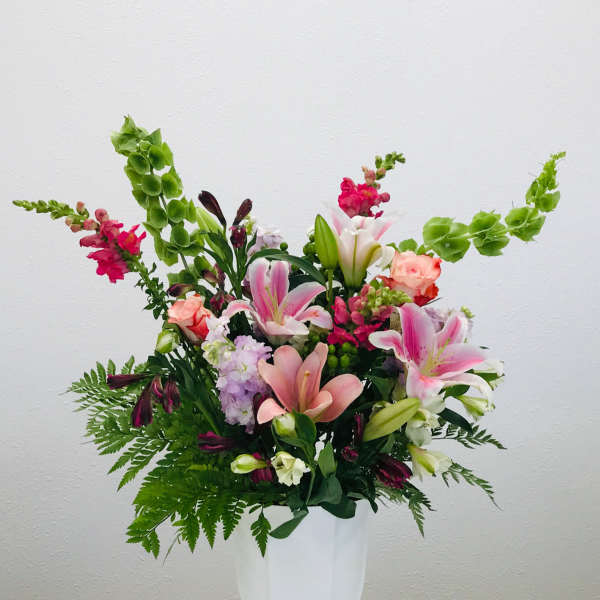 Mixed pink and white floral arrangement in a white pedestal vase