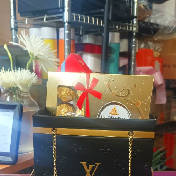 Gift bag with chocolates and a gold card, with white flowers in the background.