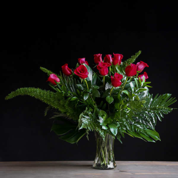 Red roses arranged in a clear glass vase with lush greenery