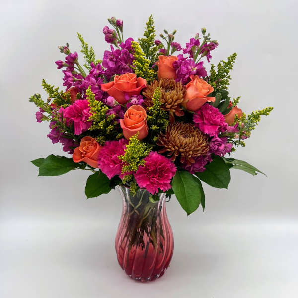 Bouquet of orange roses, pink flowers, and chrysanthemums in a pink glass vase