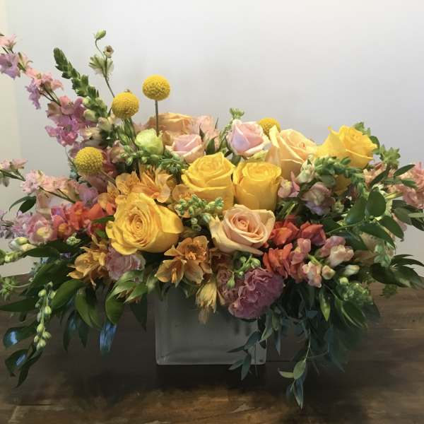 Mixed bouquet of yellow and pink roses in a low white container