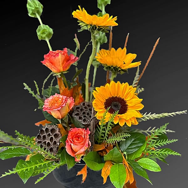 Arrangement of orange roses and yellow sunflowers in a dark vase