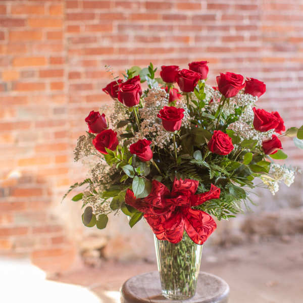 Red roses arranged in a clear glass vase with a red ribbon