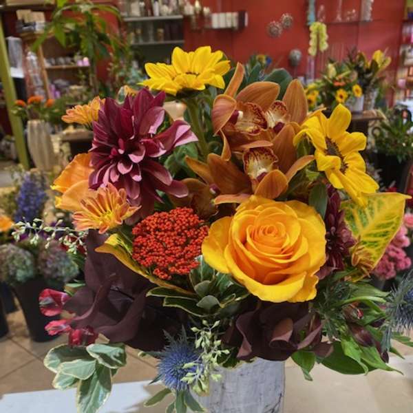 Mixed bouquet with yellow roses, sunflowers, and orchids in a white vase