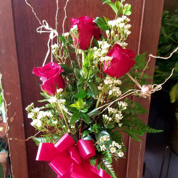 Red roses in a clear glass vase with a pink ribbon bow