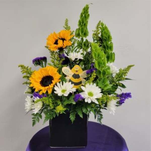 Sunflowers and daisies in a black container with a small bee decoration