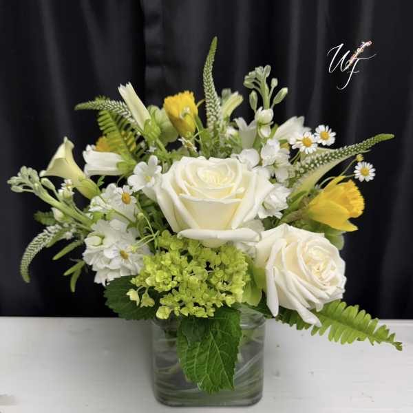 White roses and yellow flowers in a clear glass vase