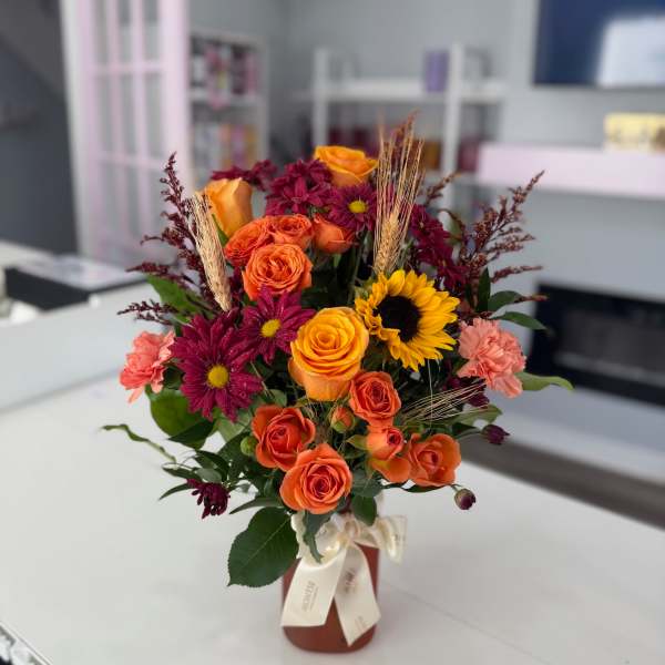 Bouquet of orange roses, burgundy daisies, and a sunflower in a vase
