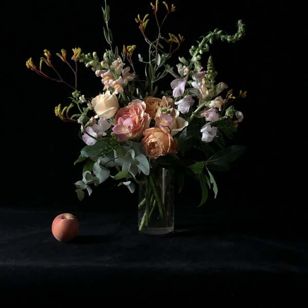 Peach and blush roses in a clear glass vase with airy greenery
