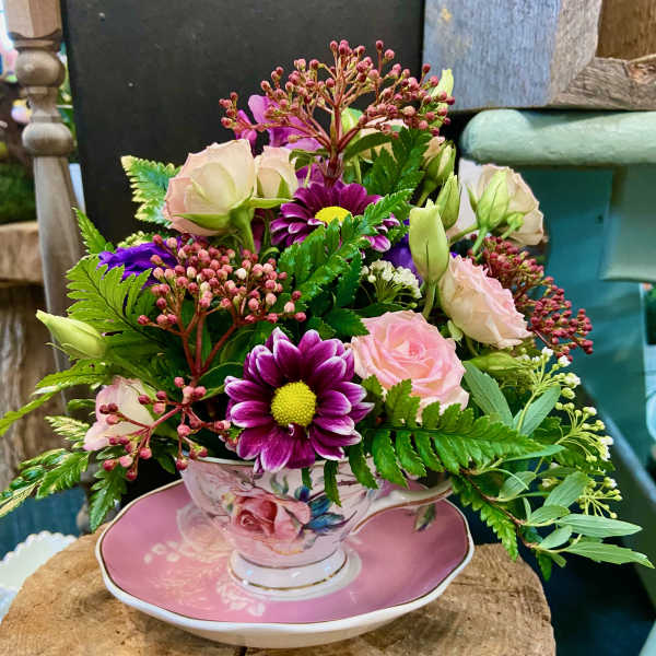 Pink and purple flower arrangement in a floral teacup and saucer