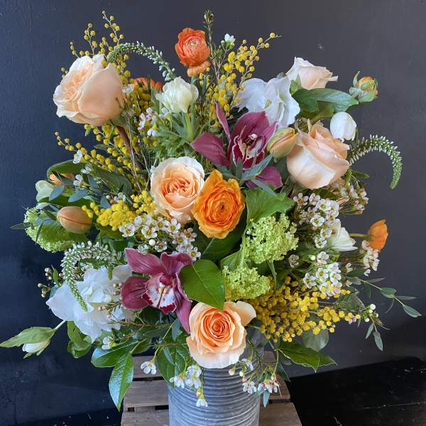Mixed bouquet of peach roses, orchids, and white blooms in a metal vase