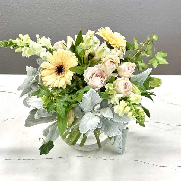 Mixed bouquet of pale roses, gerbera daisies, and white blooms in a glass vase