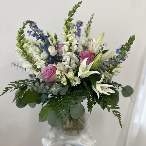 Mixed bouquet of white lilies, pink roses, and blue flowers in a glass vase