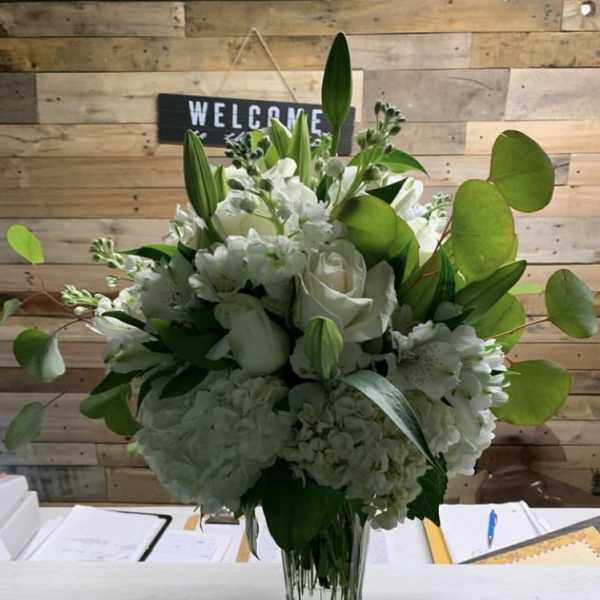 White floral arrangement in a clear glass vase with green foliage