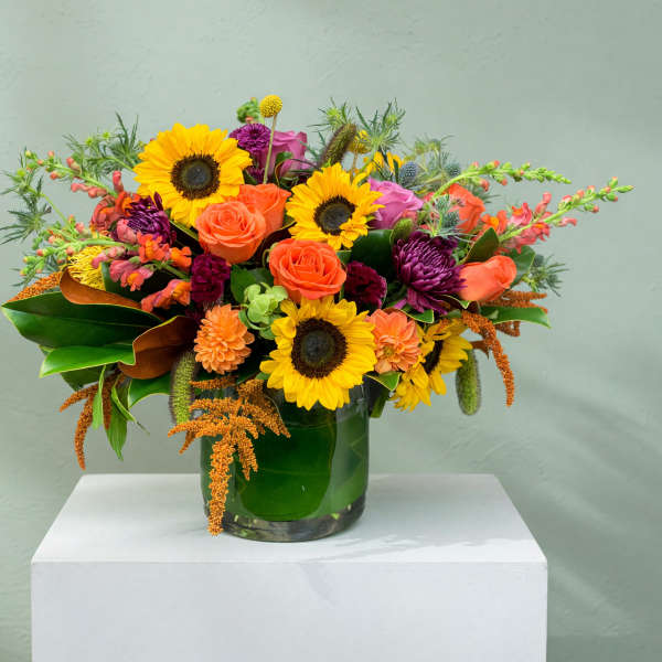 Bright mixed bouquet with sunflowers, roses, and purple blooms in a glass vase