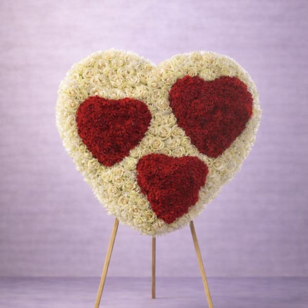 Large heart-shaped floral display of cream roses with three red heart accents on a wooden easel.