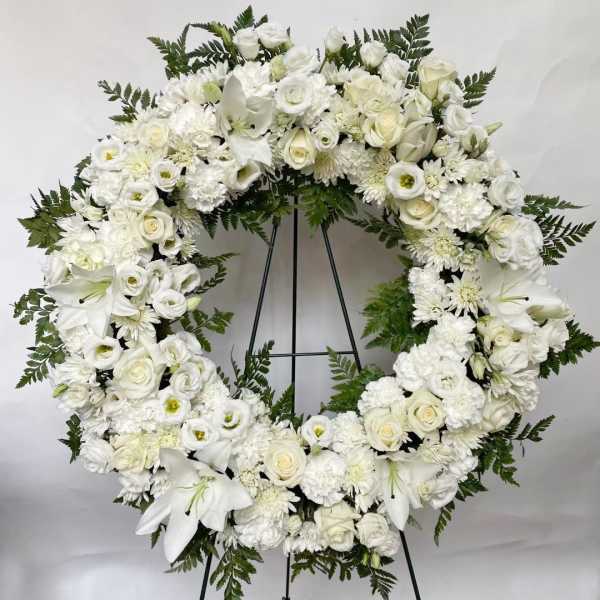 White floral funeral wreath on a black stand