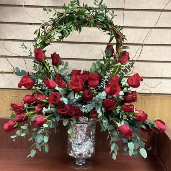 Red roses arranged in a tall vase with a leafy arch above