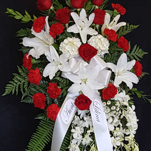 Red roses and white lilies arranged with a white ribbon on a black stand