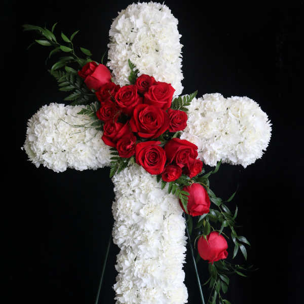 White floral cross with red roses on a black stand