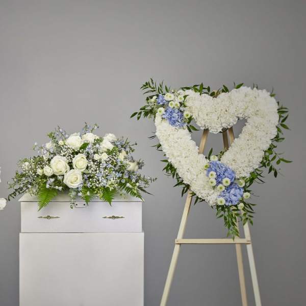 Three white floral arrangements with blue accents, including a heart wreath on an easel