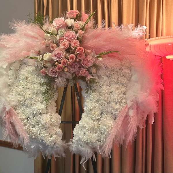 Pink and white floral wreath on an easel with feather accents