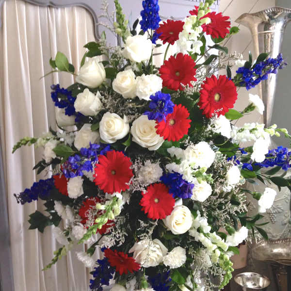 Large standing floral spray with red gerberas, white roses, and blue flowers