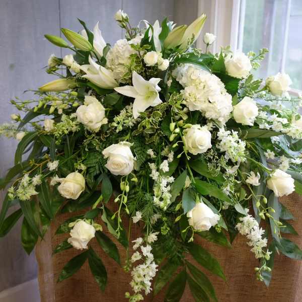 White floral arrangement with roses and lilies on a burlap-covered stand
