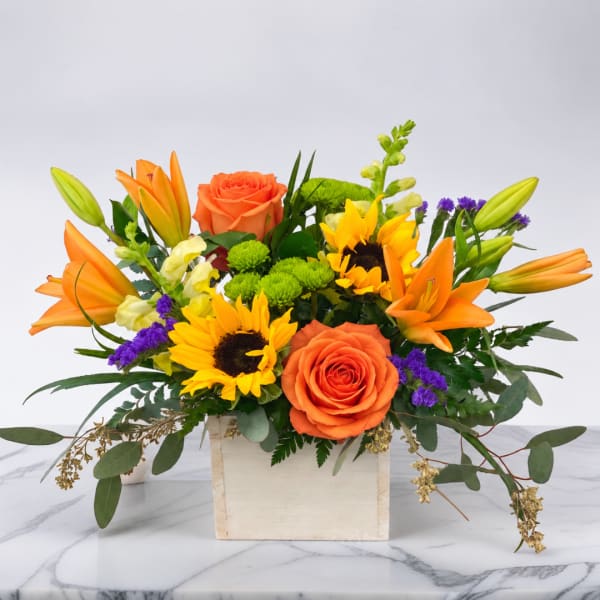 Orange roses and sunflowers in a wooden box with purple accents