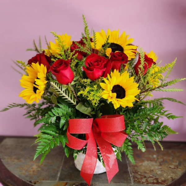 Bouquet of red roses and yellow sunflowers with a red ribbon in a white vase