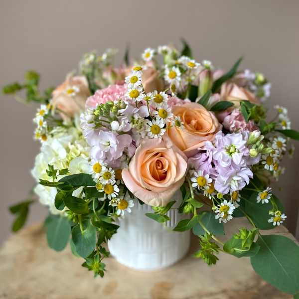 Peach roses and pastel flowers arranged in a white vase