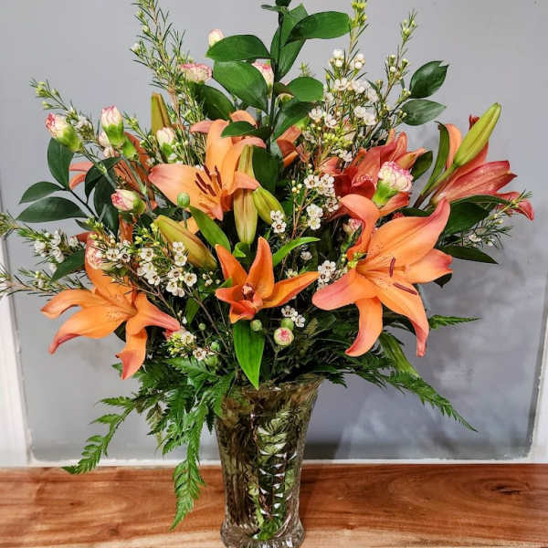 Orange lilies arranged in a clear vase with white filler flowers