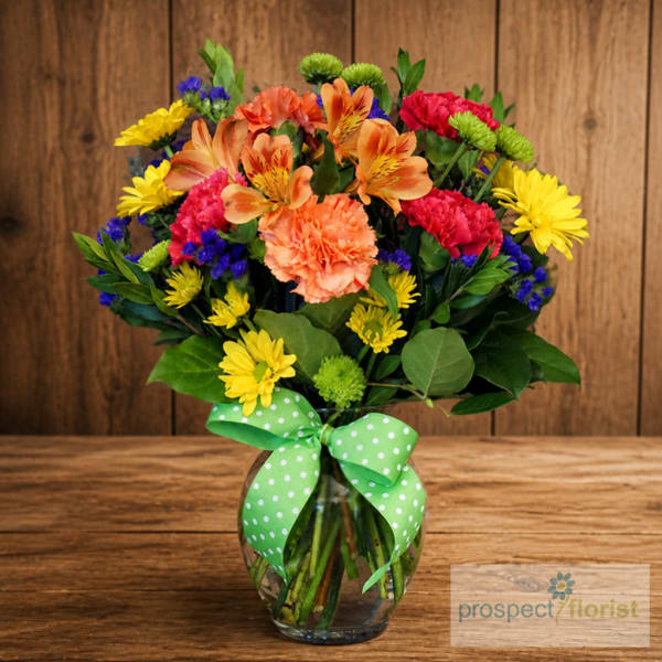 Colorful mixed bouquet in a glass vase with a green polka-dot ribbon