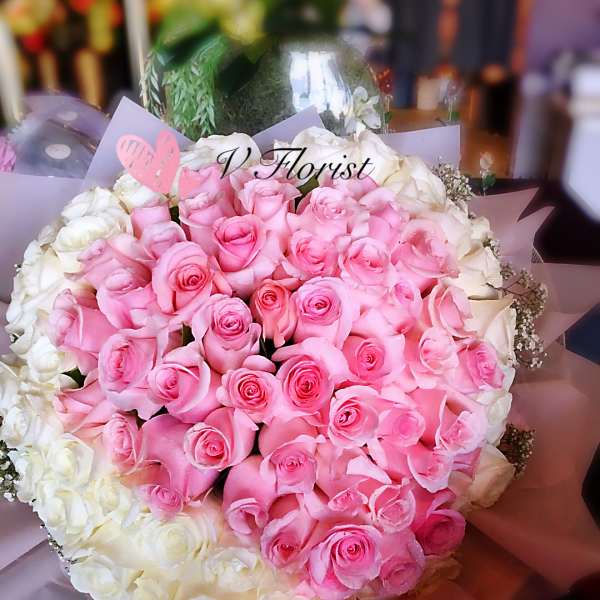 Large round bouquet of pink roses encircled by white roses in pastel wrapping paper