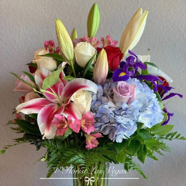 Mixed bouquet of lilies, roses, hydrangeas, and irises in a tall clear glass vase