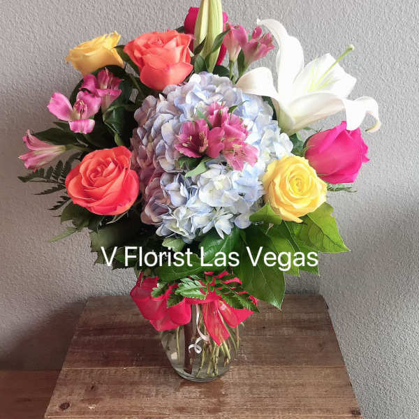Bright mixed bouquet of roses, lilies, hydrangea and alstroemeria in a clear glass vase on a wooden crate.