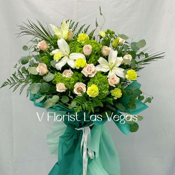 Bouquet of white lilies, pale roses, and green hydrangeas wrapped in teal paper