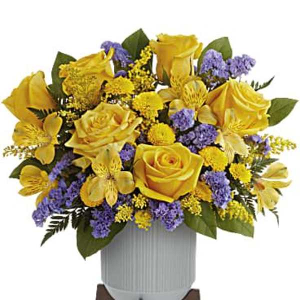 Yellow roses and purple filler flowers arranged in a white vase