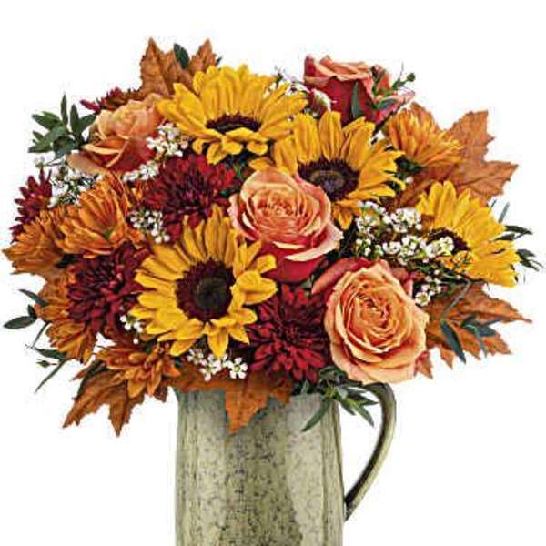 Bouquet of sunflowers, roses, and autumn flowers in a ceramic pitcher