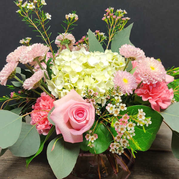 Low arrangement of pink roses, carnations, mums, and white hydrangea in a round glass vase