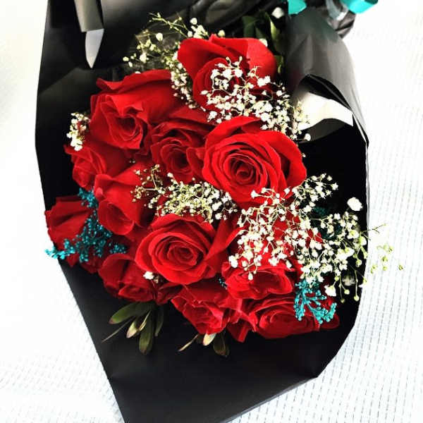 Bouquet of red roses wrapped in black paper with a teal ribbon