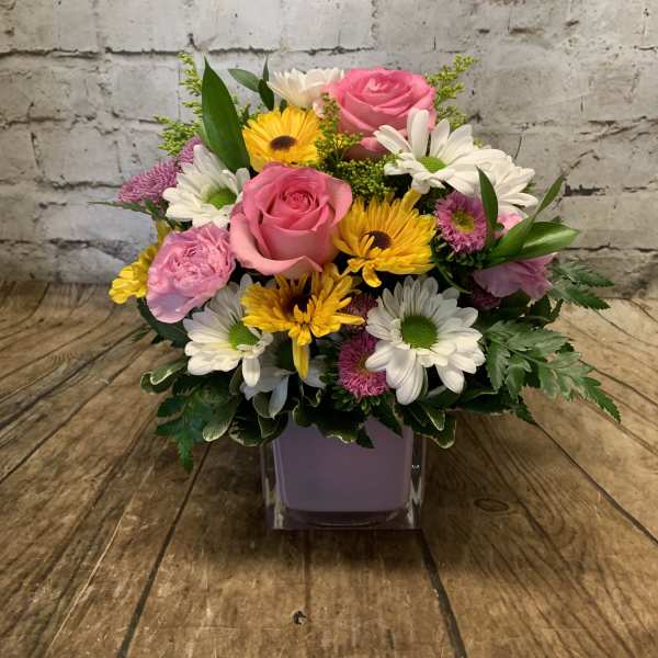 Mixed bouquet of pink roses, daisies, and yellow flowers in a square vase