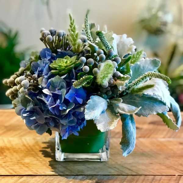 Blue and green floral arrangement in a square glass vase